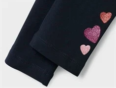 Nærbillede af glitrende hjerter i pink og rød på mørkeblå Name It leggings ved bukseben